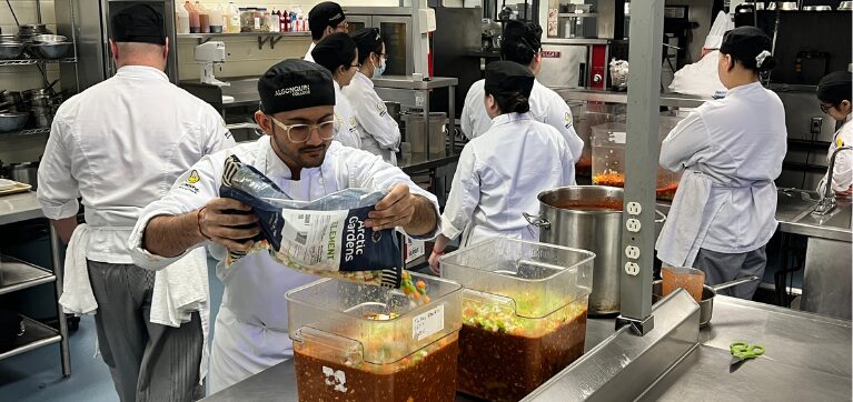 A student adds a vegetable mix to the chilli.